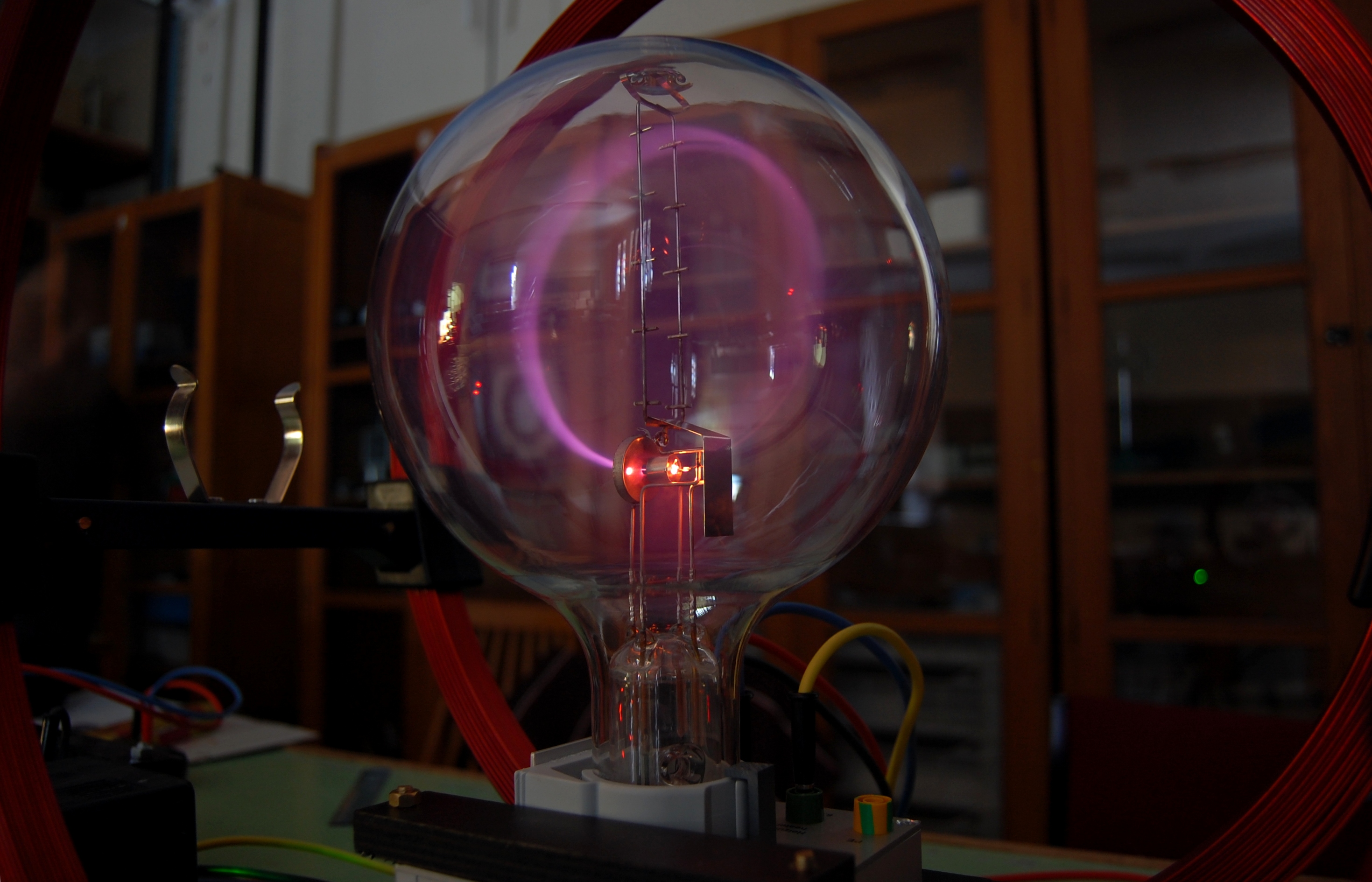 A vacuum bulb apparatus containing a jet of charged particles emitting a purple glow; the particles are seen to move in a circular trajectory due to an external electromagnetic field.